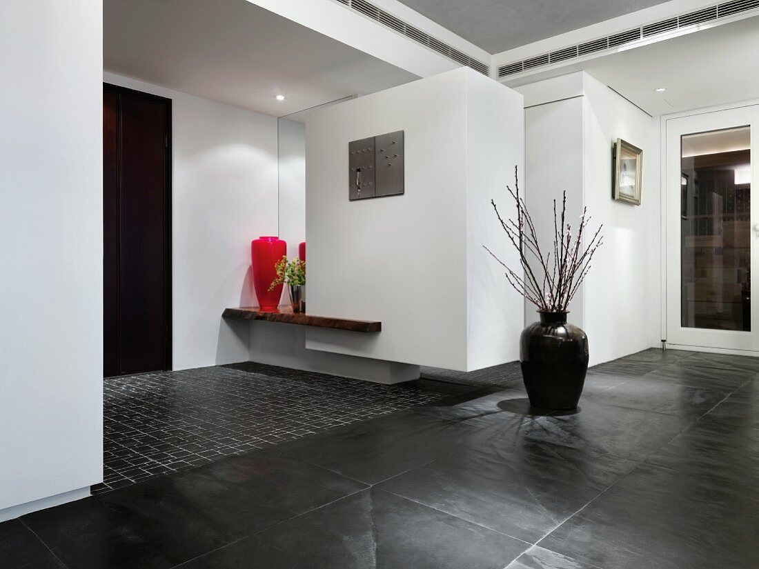Bodenvase mit Zweigen auf dunkelgrauen Schieferboden im minimalistischen Vorraum