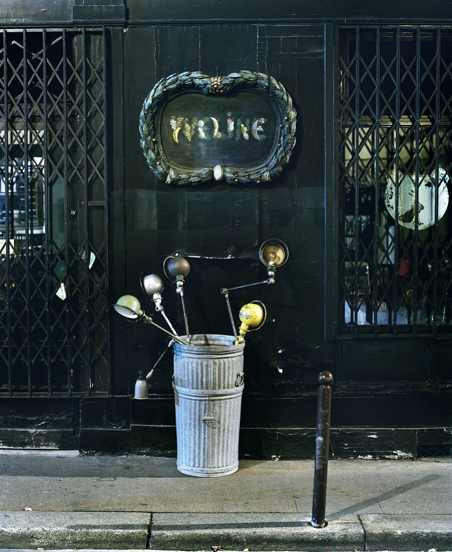 Sammlung von Vintage Tischleuchten aus Metall im Eimer vor altem Geschäft mit geschlossenem Fenstergitter