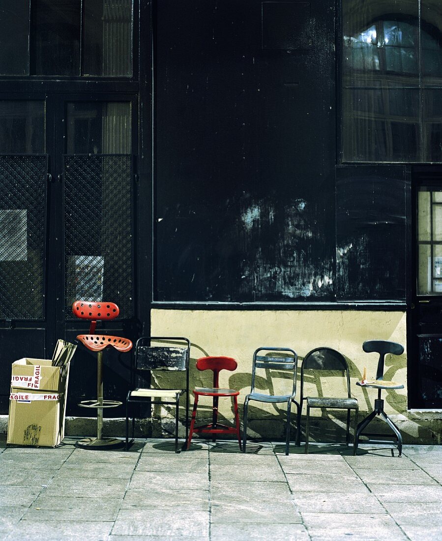 Various vintage metal chairs on pavement in front of shop