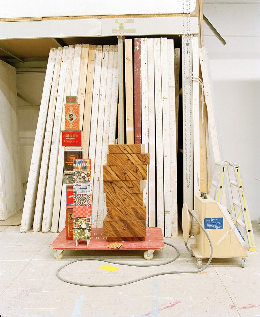 Stacked drawers next to colourful paper boxes on dolly in front of stock of wooden partition walls (furniture dolly)