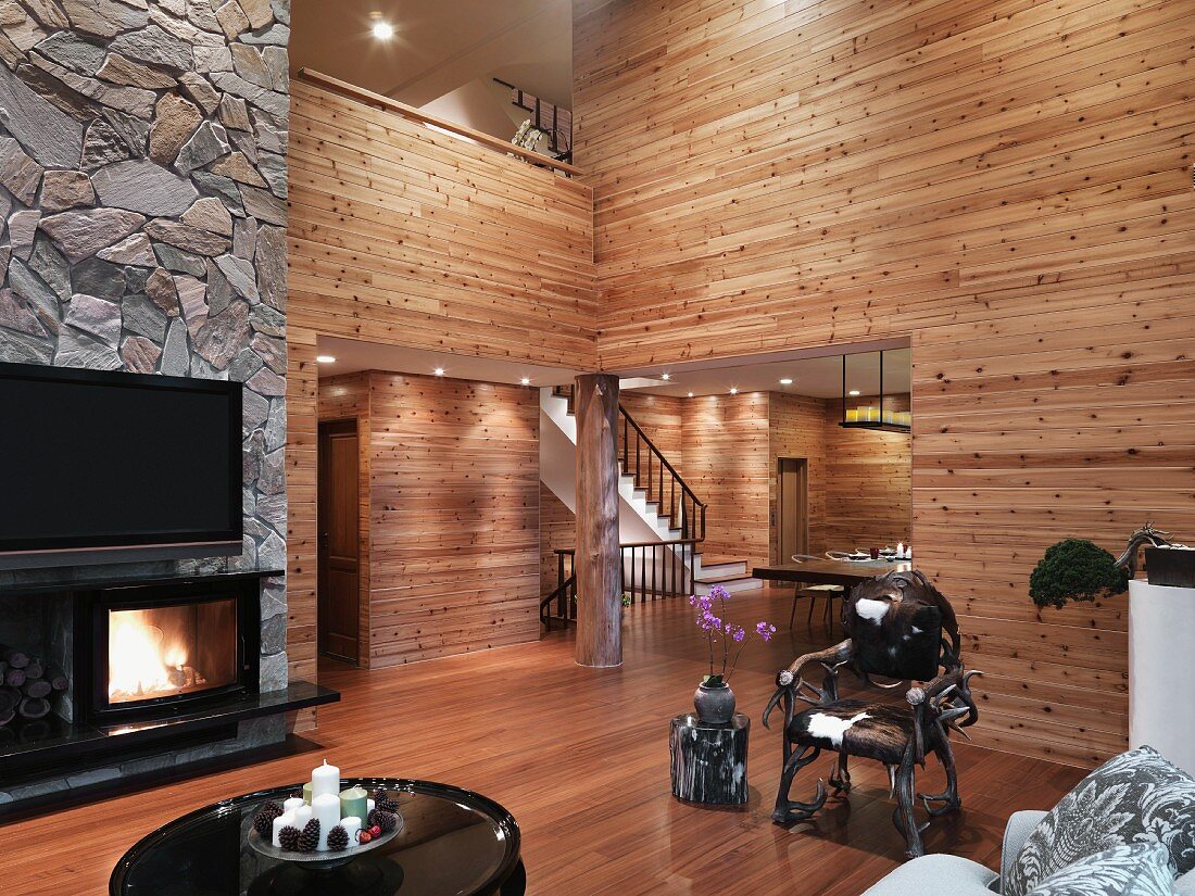 Minimalist living room with wood paneled walls and open fireplace under a TV on a natural stone wall