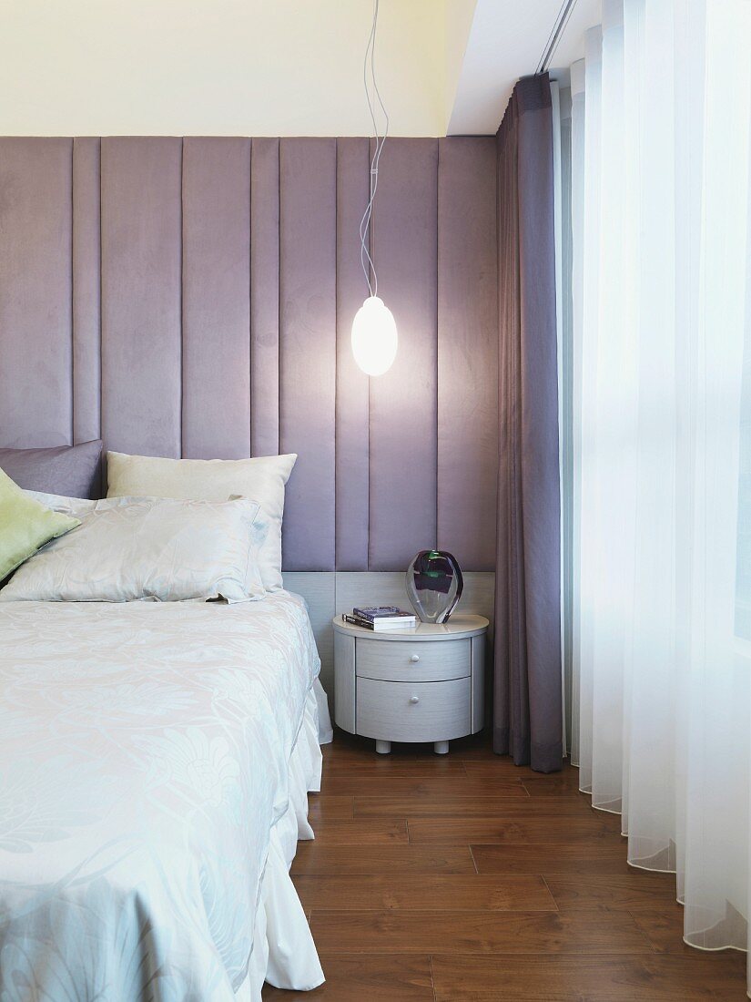 Modernes Schlafzimmer mit Doppelbett und Nachtkästchen vor gepolstertem Wandpaneel