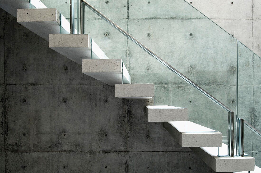Treppe mit hellen Steinstufen und Vollglas Geländer an Betonwand befestigt