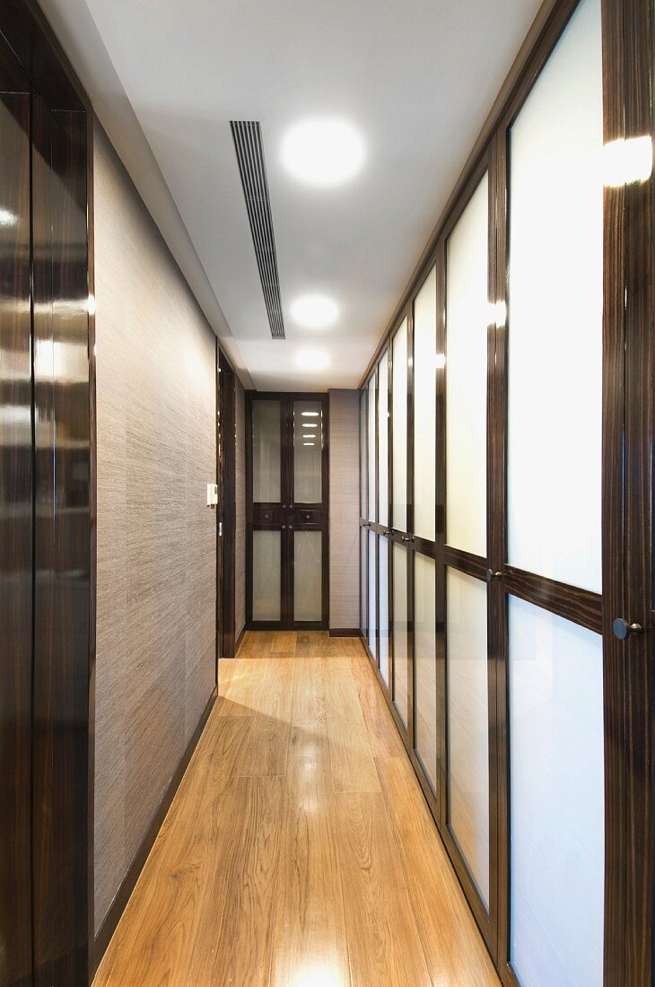Modern, narrow hallway with a partition wall made of opaque glass framed in wood