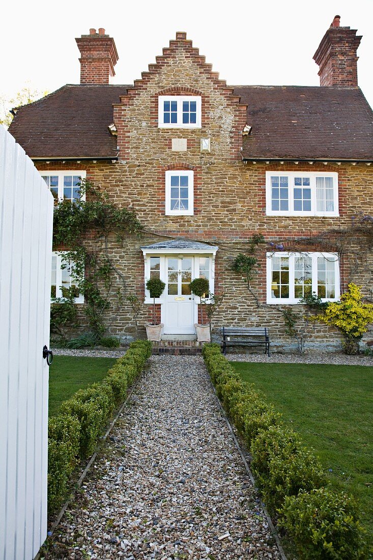 Gekiester, mit Buchs gesäumter Zugangsweg eines alten, englischen Landhauses mit Ziegelfassade und weißen Sprossenfenstern.