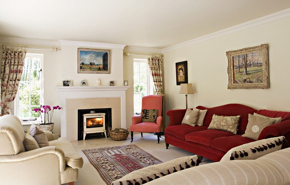 Verschiedene traditionelle unifarbene Polstermöbel in hellem Wohnraum mit Kamin und Landschaftsmalerei; gerafften Vorhängen und einer Teppichbrücke mitten im Raum.