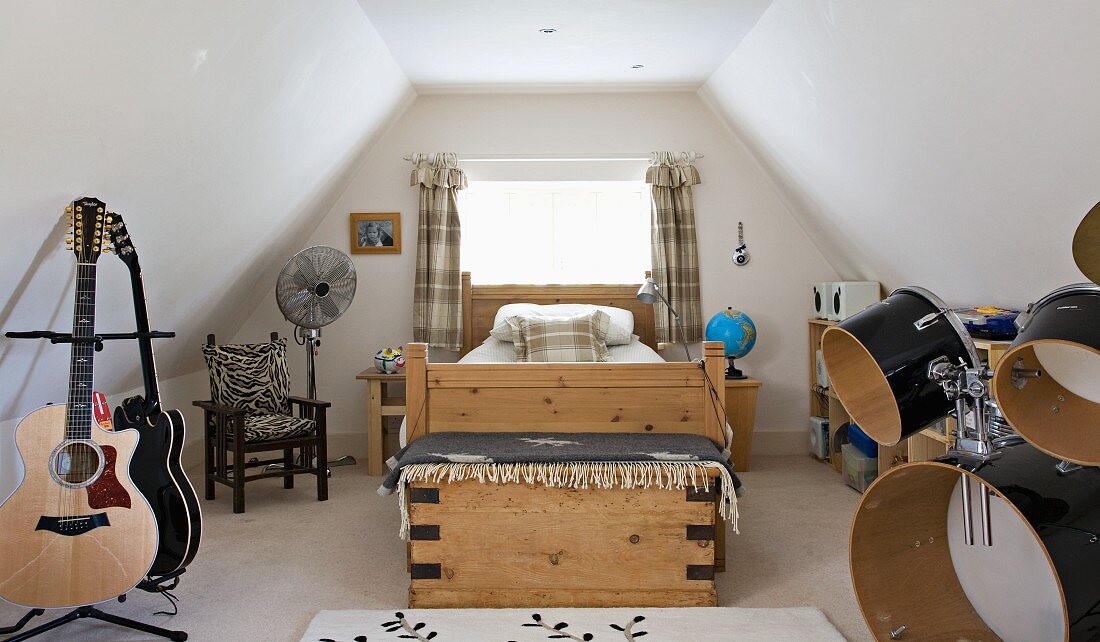 Youthful, country-house style in attic bedroom with wooden bed, guitar stand and drum kit
