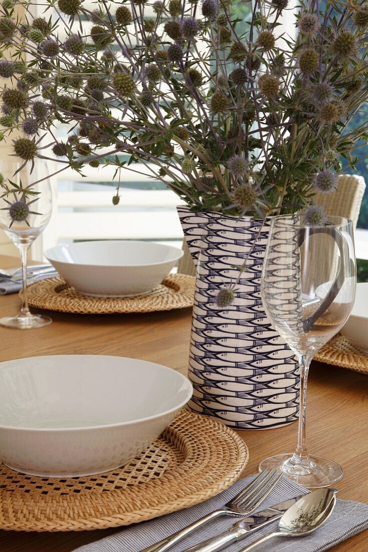 Festlich gedeckter Tisch mit Trockenstrauss in dekorativem blau-weißem Keramikkrug und weiße Suppenteller auf geflochtenen Sets