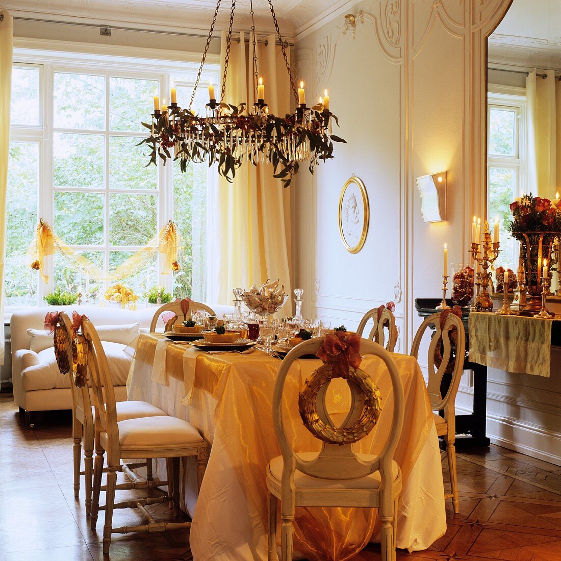 Festively set table below chandelier with lit candles in grand interior