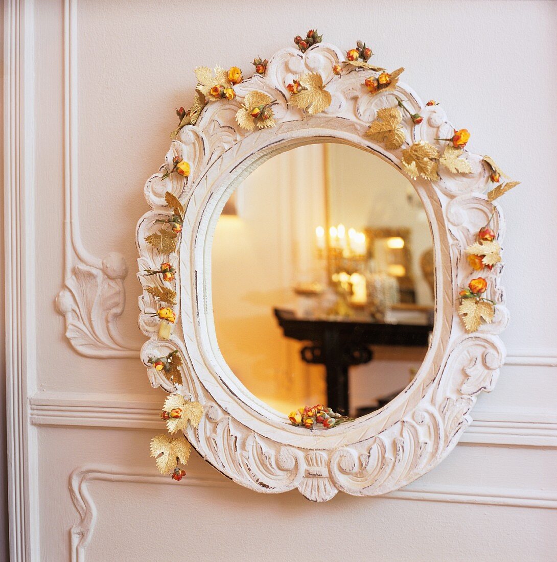 Reflexionen im Wandspiegel mit Blumendeko auf weißem geschnitzten Rahmen an weisser Wandverkleidung aus Holz