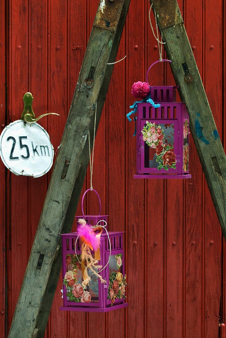 Lilafarbene Laternen mit Blumenkarten an alter Leiter vor roter Holztür