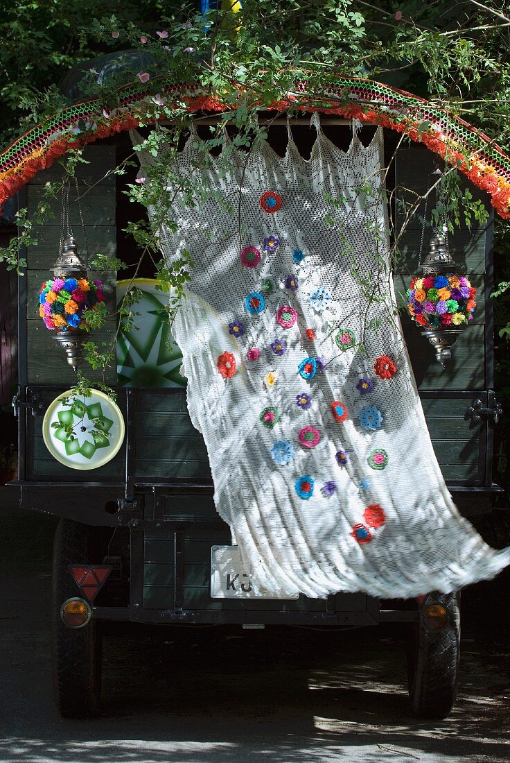 Wehender Vorhang mit applizierten Blütenmotiven und bunte Häkelbordüre als Schmuck an einem Fahrzeug