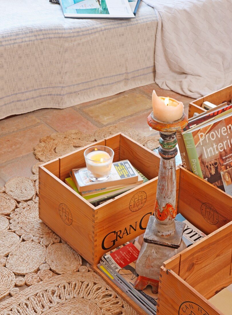 Lit candle on candlestick amongst crates of books on floor