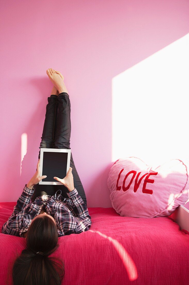 Junge Frau liegt mit einem Tablet-PC auf dem Bett