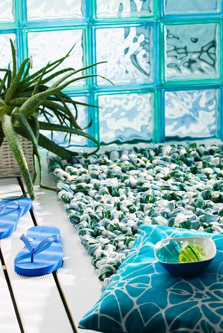Green and white looped bathmat in front of turquoise glass brick wall
