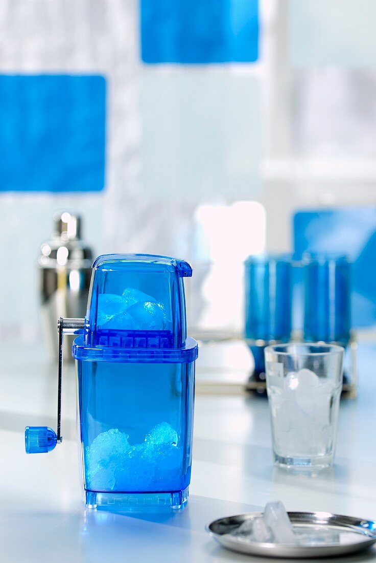 Blauer Eiscrusher und Glas mit Eiswürfeln