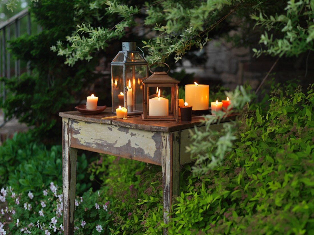 Brennende Kerzen & Laternen auf Tisch im Garten