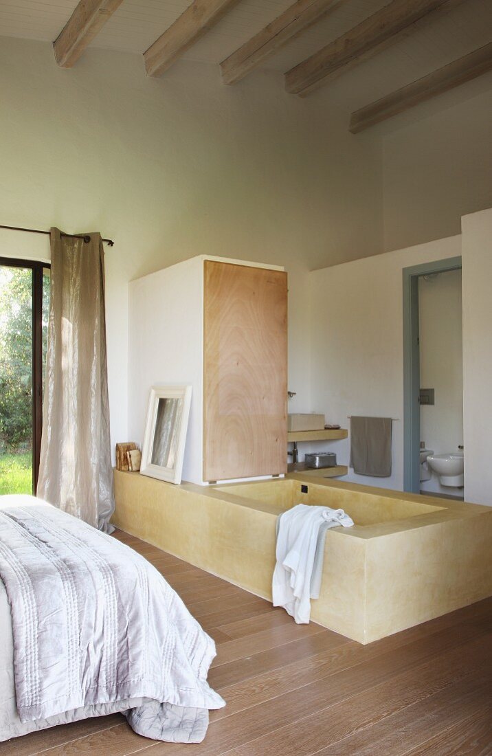 Free-standing bathtub in front of separate lavatory in simple bedroom