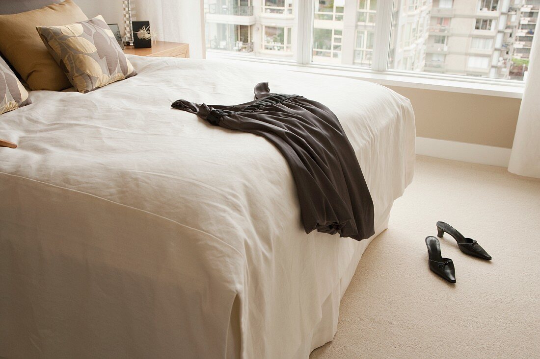 Ausgebreitetes, schwarzes Kleid auf einem Bett mit weißem Überwurf