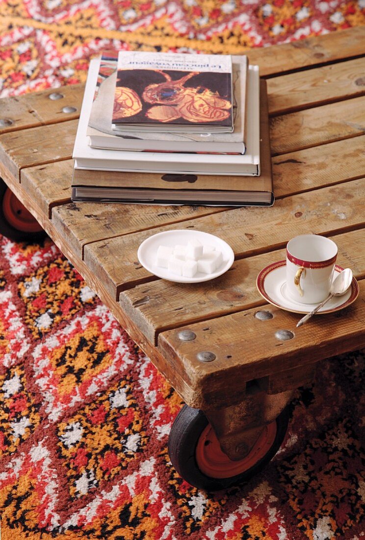 Mokkatässchen und Untertasse mit Zuckerwürfeln auf rollbarem Bodentisch aus Holz und gemusterter Teppich