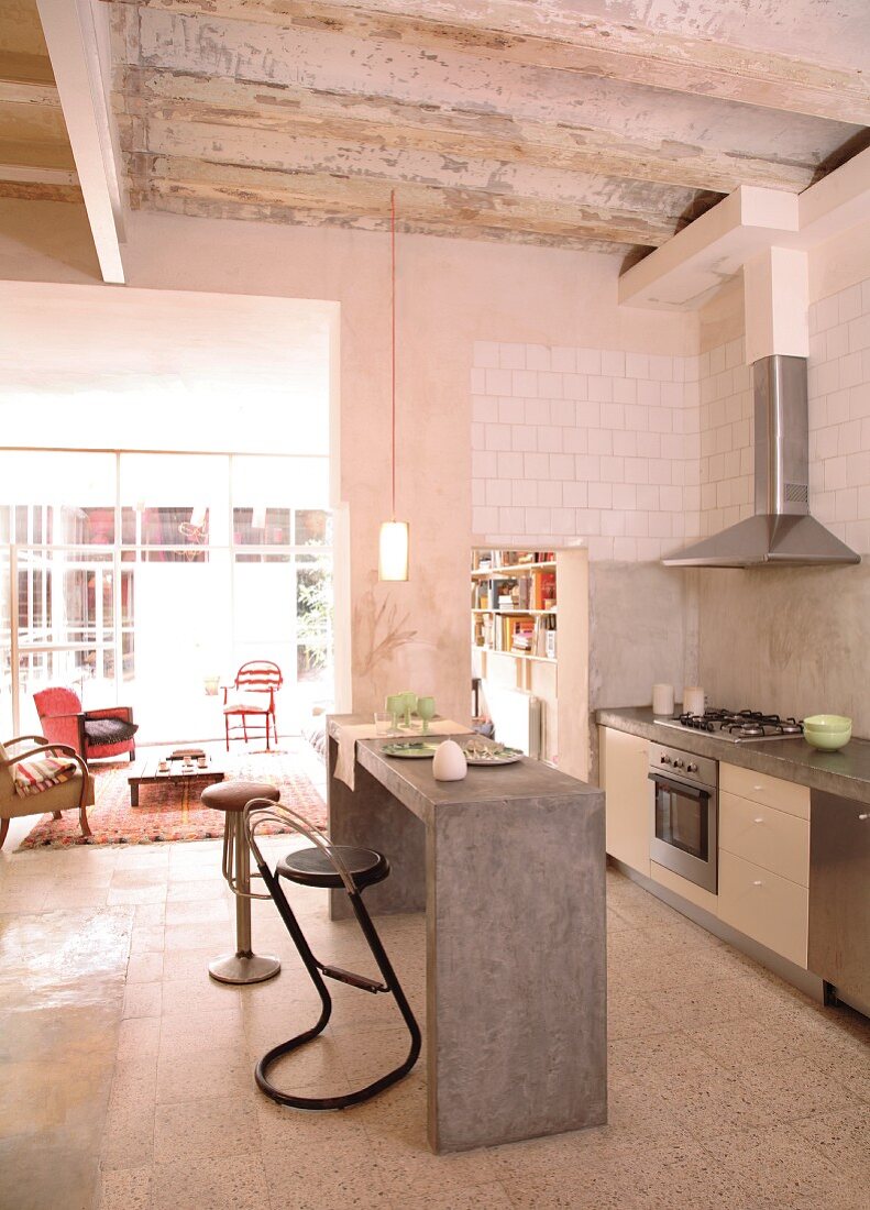 Theke aus Beton und Barhocker in offener Küche vor breitem Durchgang mit Blick in Wohnbereich eines Lofts
