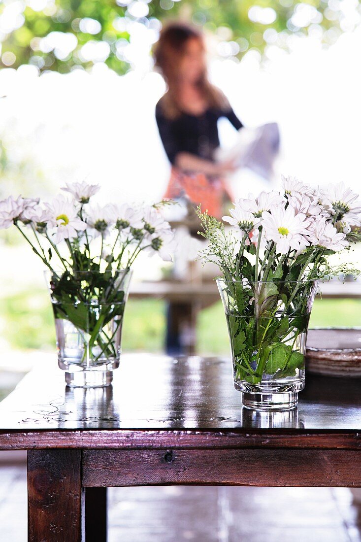 Posies of white flowers in water glasses on glossy wooden table on terrace