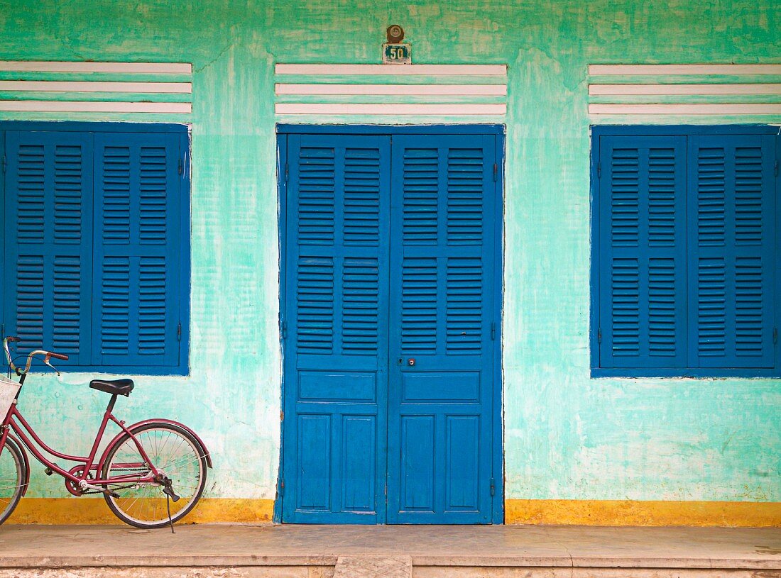 Grüne Hausfassade mit verschlossenen, blauen Fenster- und Türläden; davor ein Fahrrad