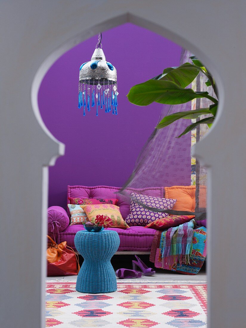 View of blue wicker table and mattress sofa in interior with Oriental ambiance through keyhole window