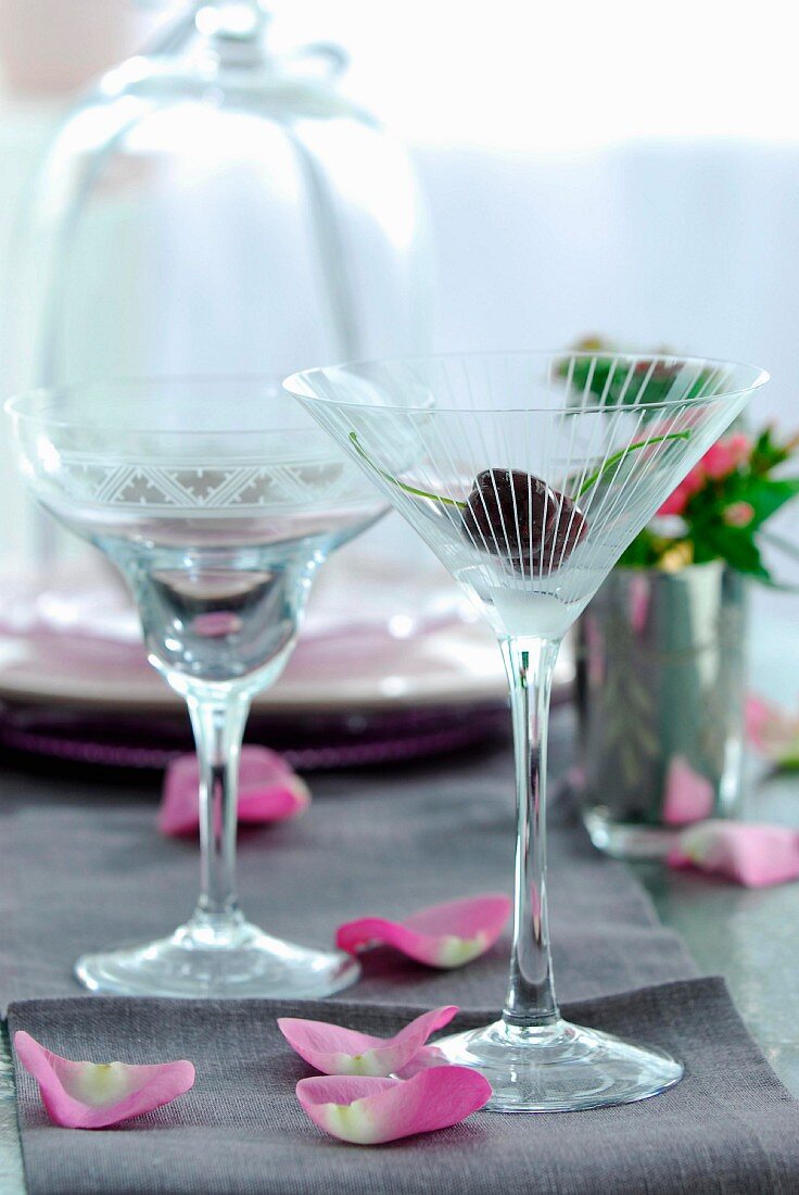 Cocktailgläser im 50er Jahre Stil und Blütenblätter auf grauem Tischläufer