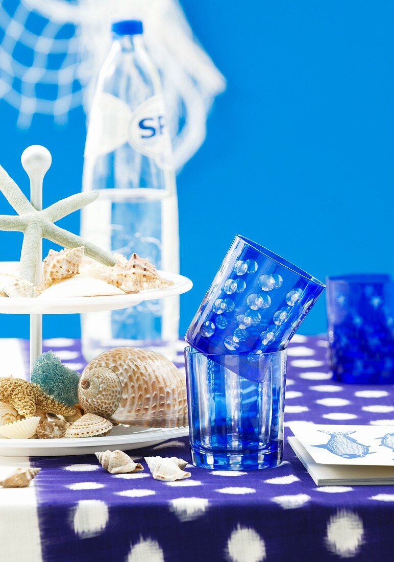 Table with blue tablecloth, blue glasses & seashells on cake stand