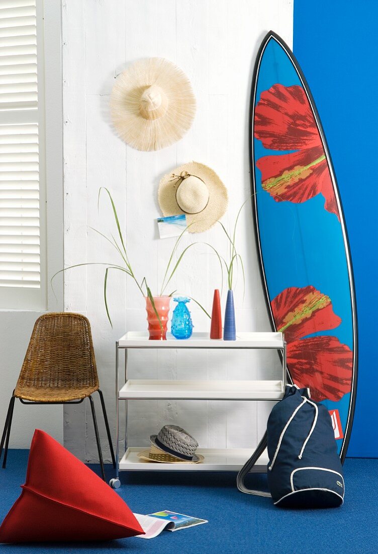 Strohhüte an Wand hängend & Surfboard neben Ablagetischchen mit Glasvasen