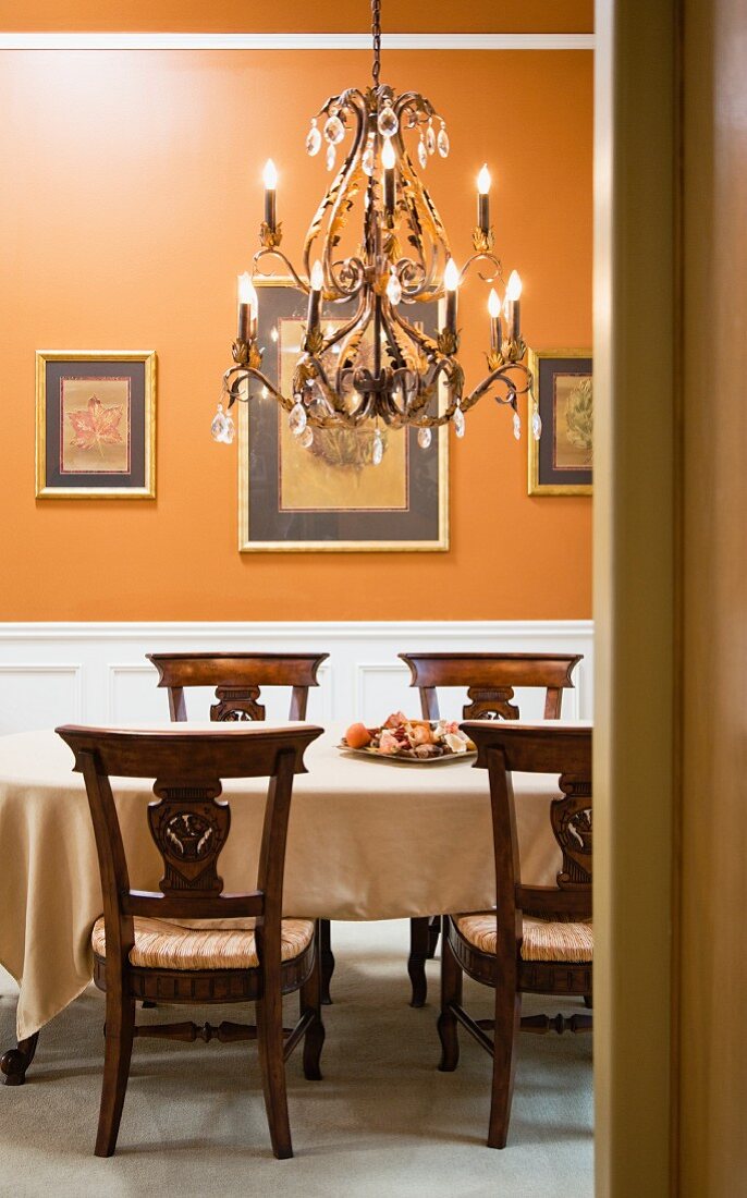 Blick in ein Esszimmer mit Kronleuchter und orangefarbener Wand