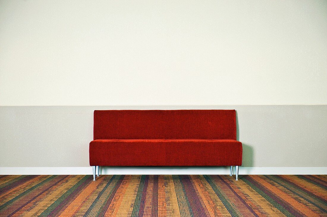 Eine rote Couch an der Wand und Teppichboden mit Streifenmuster