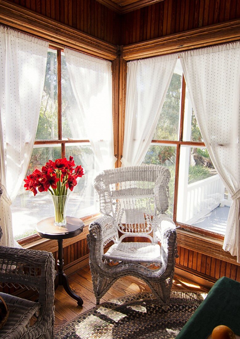 Weisser Korbstuhl am Fenster, Vase mit roten Blumen auf Beistelltisch