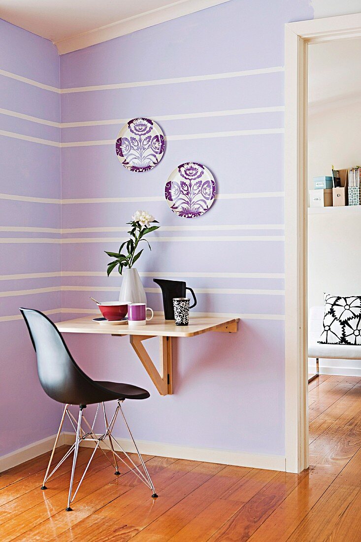 Black Bauhaus shell chair in front of console table in corner of room with lilac and white striped wall