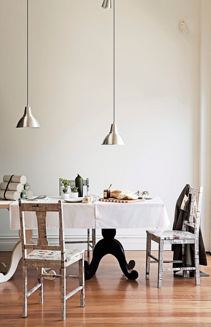 Pendel-Hängeleuchten mit Alu-Metallschirm über gedecktem Tisch mit schwarzem-weißem geschwungenem Fussgestell und schlichte, bedruckte Stühle in minimalistischem Altbau-Ambiente