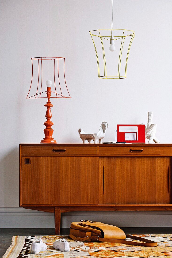 Fifties-style teak sideboard, table lamp and pendant lamp with wire frames and turned base and colourful rug in foreground