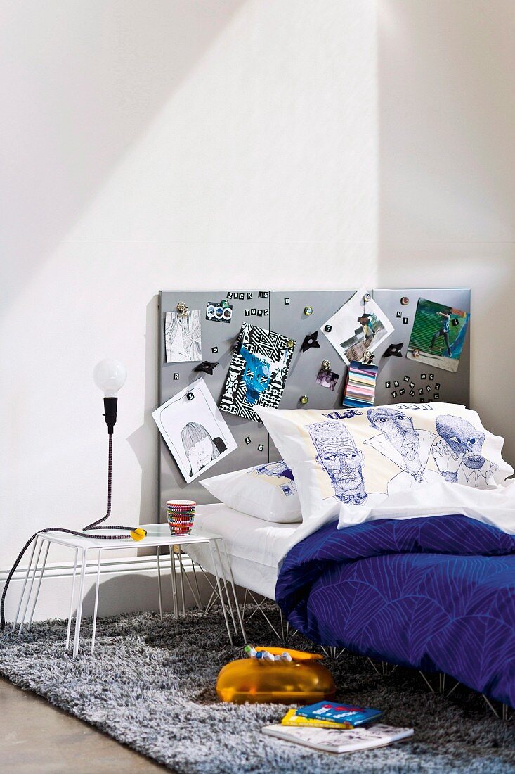 Teenager's bed and bedside table with metal frame and metal pinboard as headboard on flokati rug