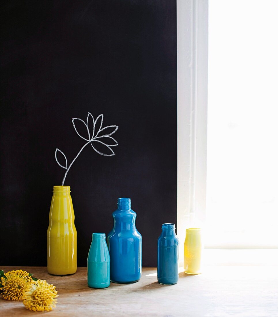 Gelbe und blaue Flaschen vor schwarzer Wand mit gezeichneter Blume