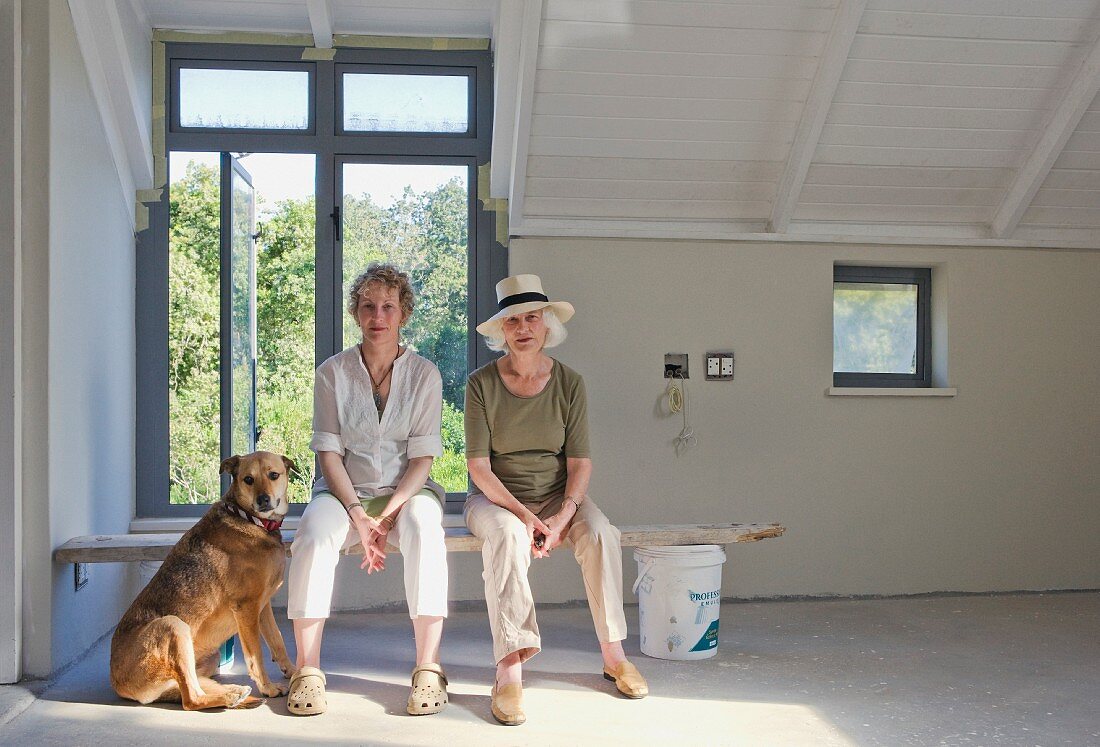Zwei Frauen mit Hund sitzen auf Holzbrett im renovierten Zimmer