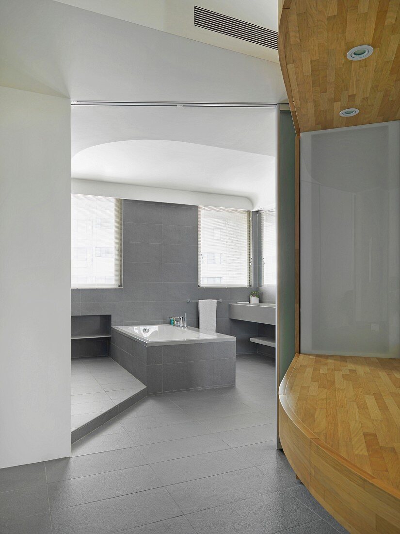 Vorraum mit Podest aus Holz und Blick in offenes Designer Bad mit grauen Steinfliesen an Wand und Boden