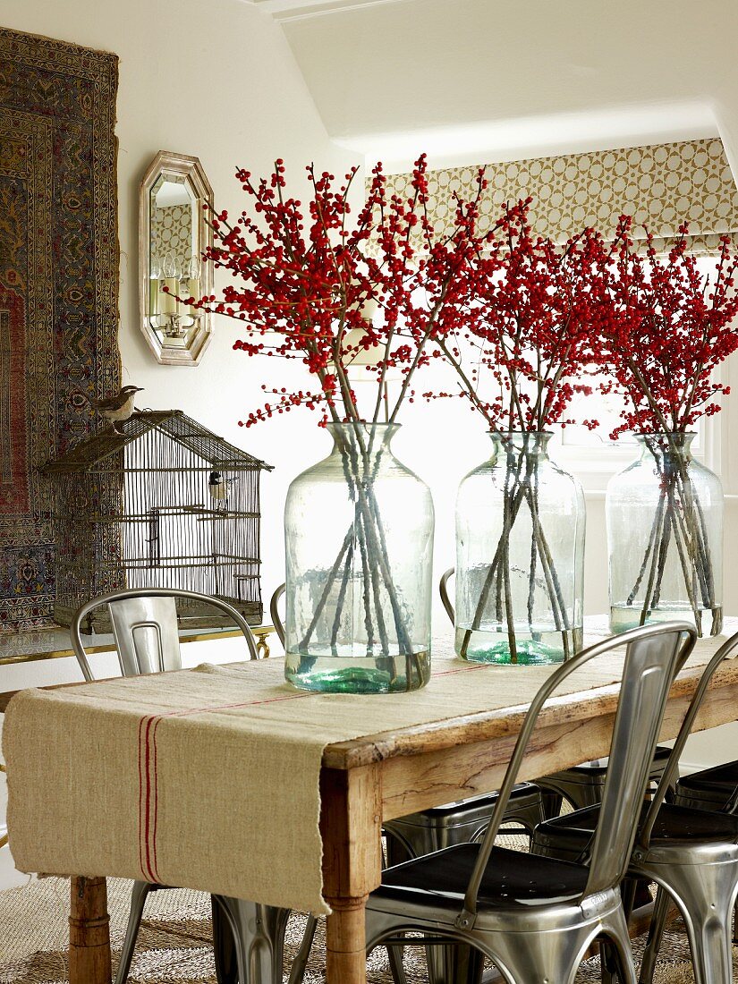 Branches of berries in glass vases on table and retro metal chairs in simple interior
