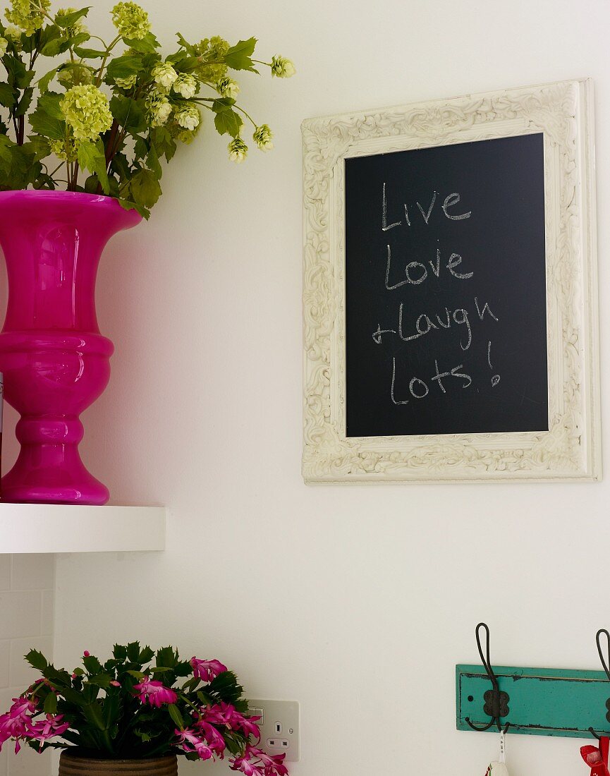 Eingerahmte Schiefertafel hängt an der Wand neben Regal mit Blumenvase und Blumentopf