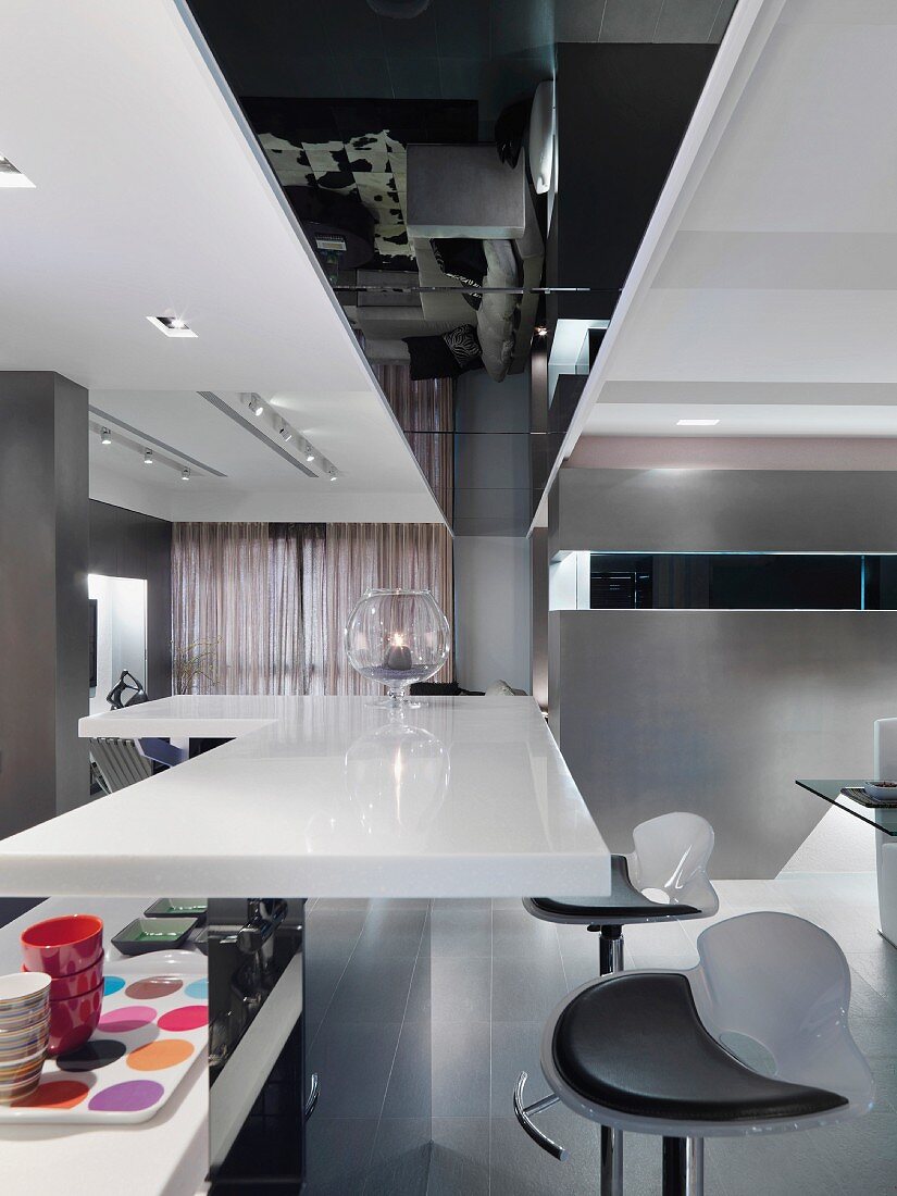 Modern, white kitchen counter and designer bar stools in an open living room