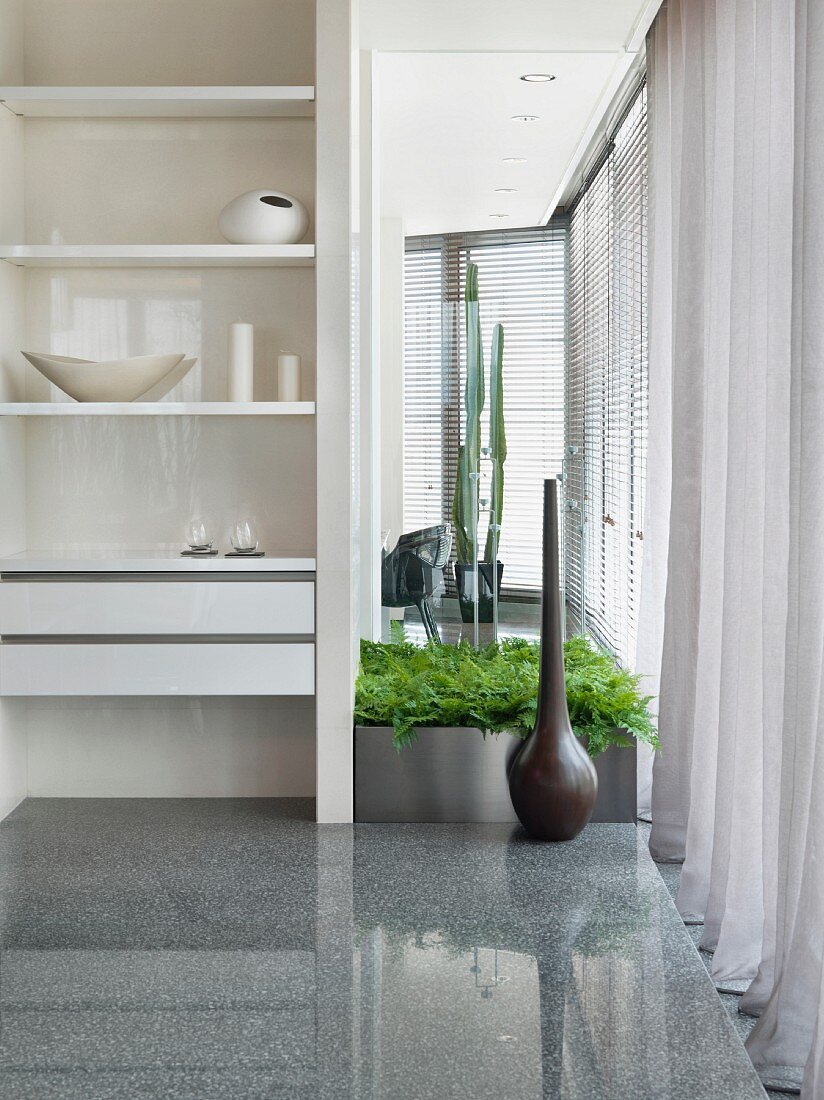 Weisser Regalschrank als Raumteiler neben Bodenvase und Pflanzenbehälter auf glänzendem Steinboden