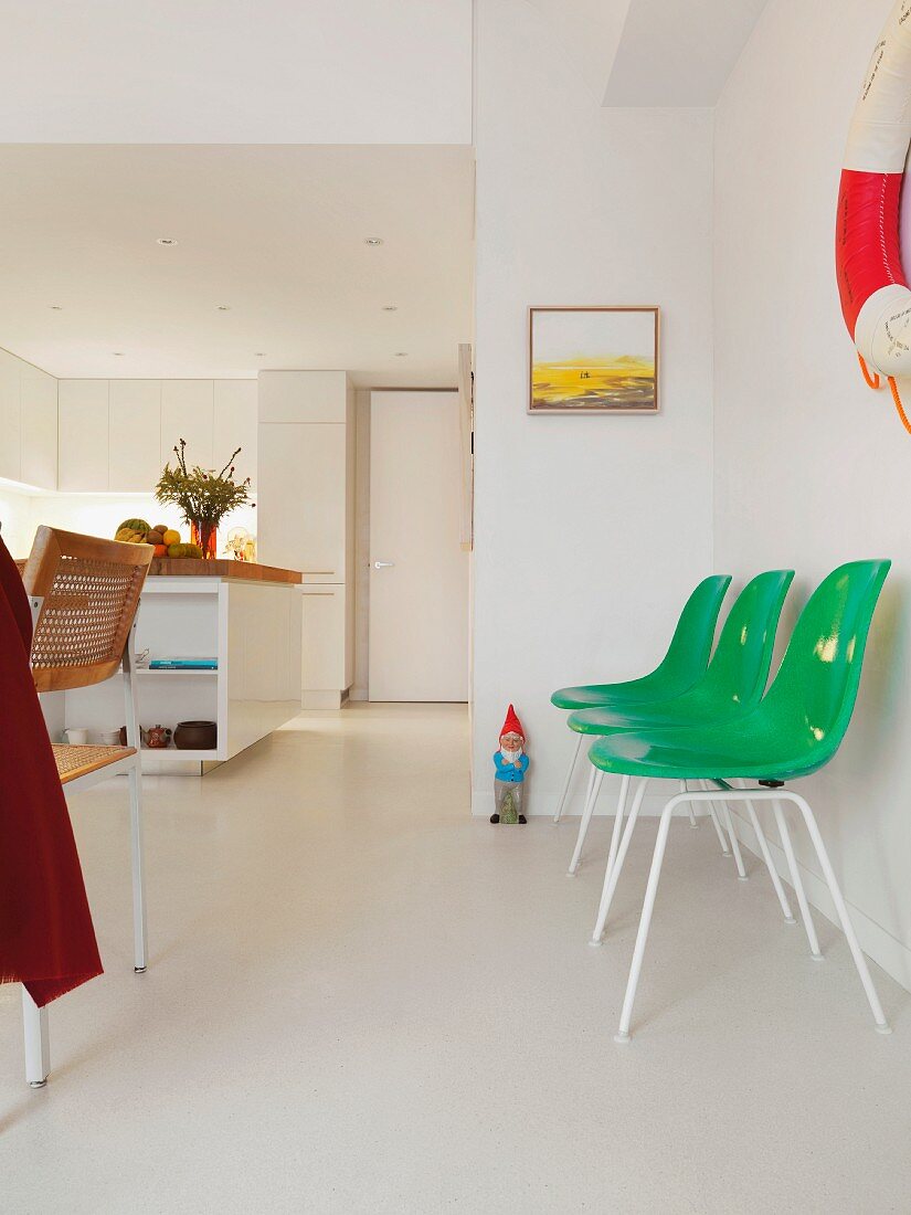Green plastic shell chairs along a wall on a white floor in an open living room