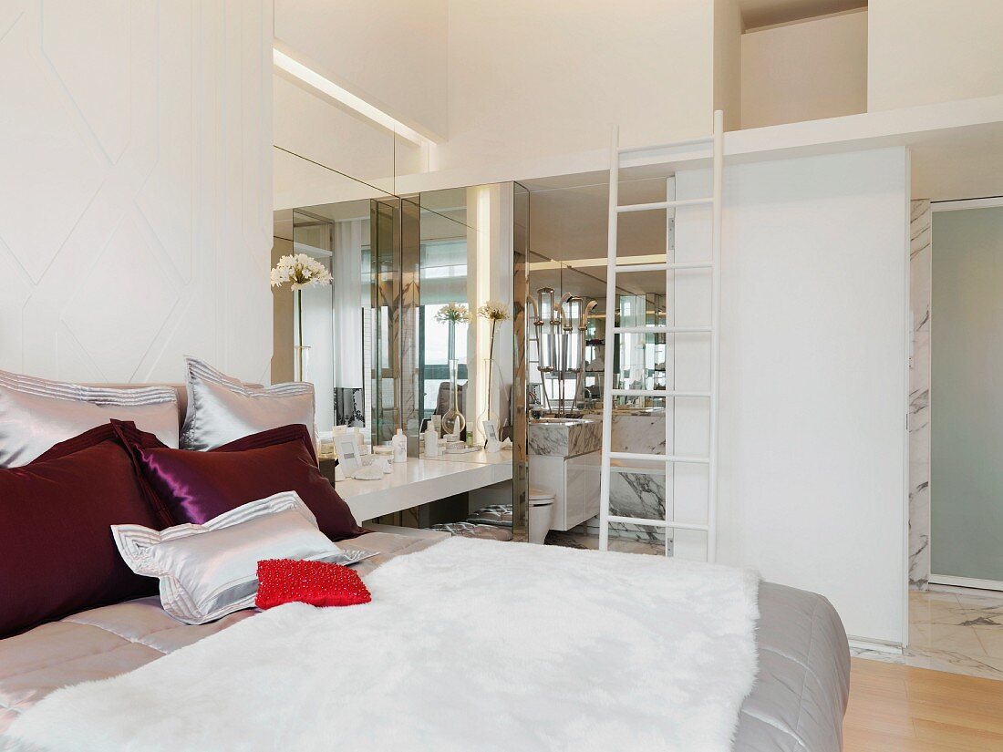 Farbige Kissen auf Doppelbett in modernem Schlafzimmer mit Blick ins Bad ensuite