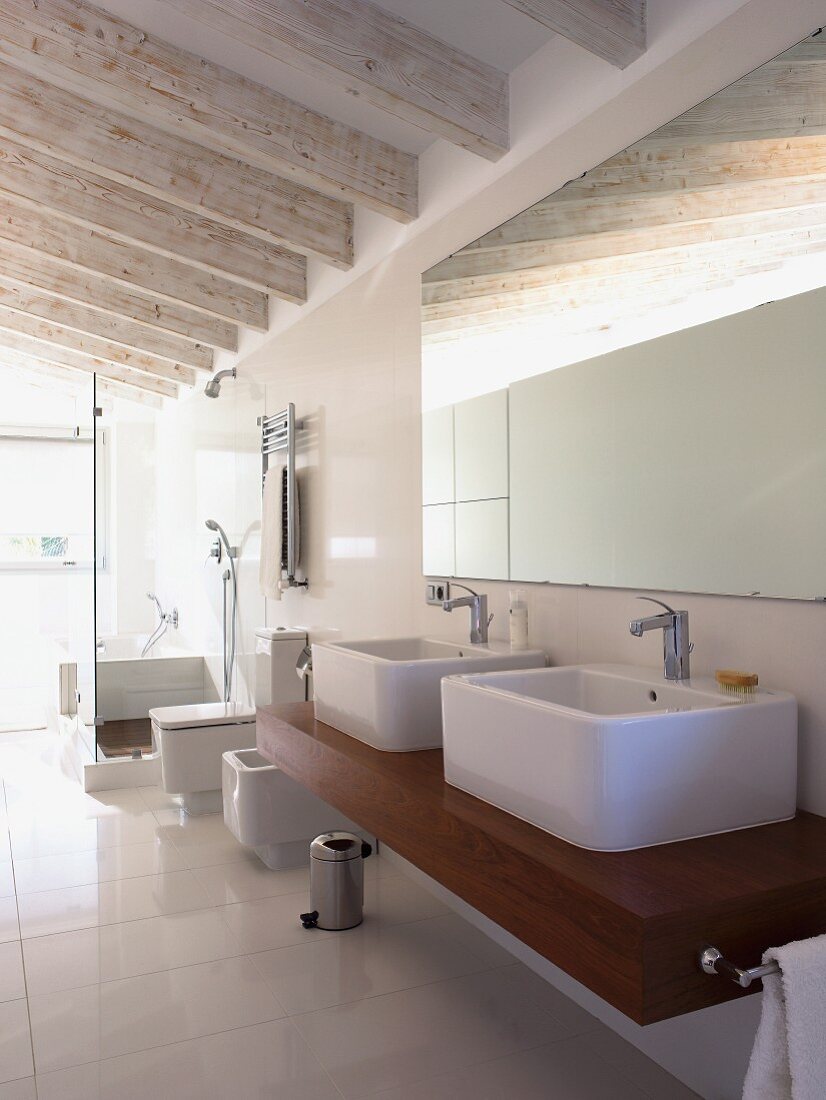 Weisses Designerbad mit lasierten Deckenbalken; wuchtige Aufsatzbecken auf massivem Holzwaschtisch