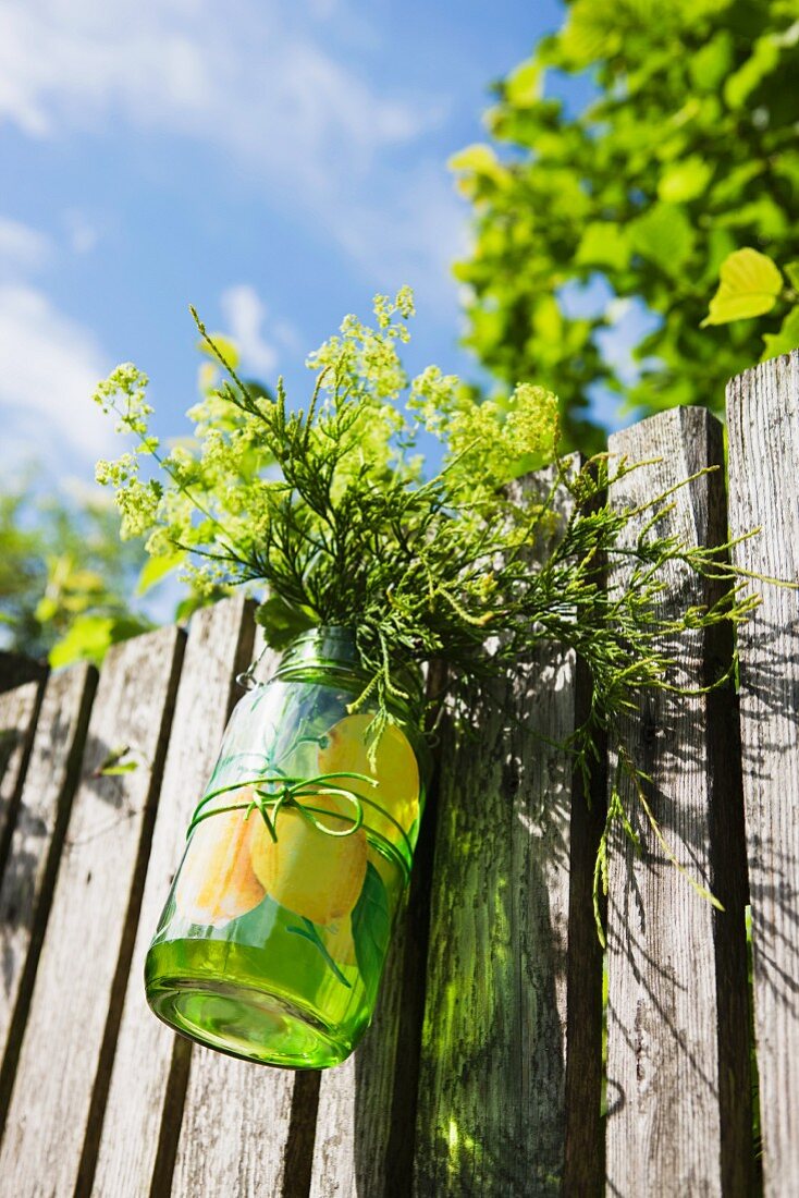 Glas mit Gartenblumen an Holzzaun gehängt