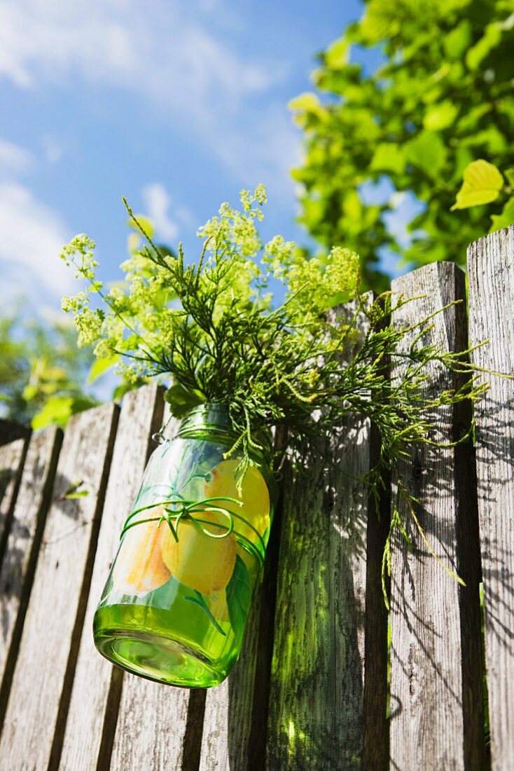 Jar of garden flowers hanging on wooden fence